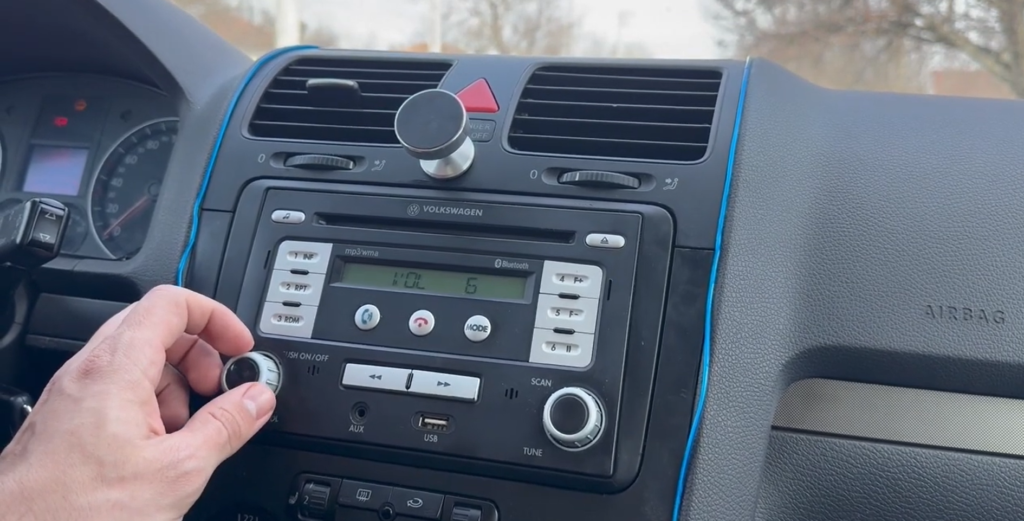 Close-up view of a hand using the tuning knob on a Volkswagen Delta 6 radio unit inside a VW Golf dashboard. The radio is locked and showing the 'SAFE' message.